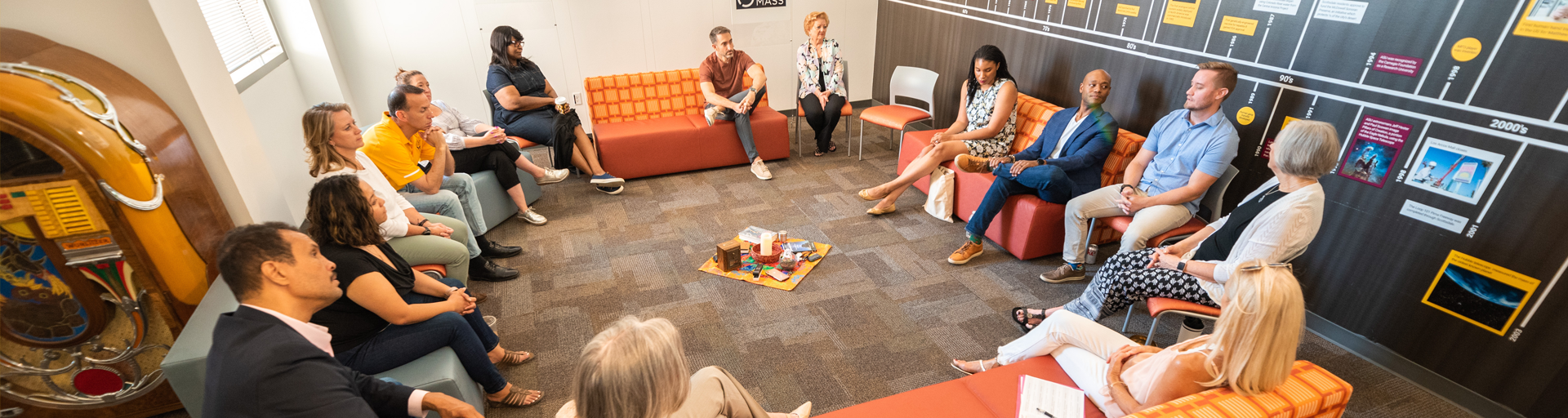 Various professionals seated facing each other while sitting in orange couches and chairs.